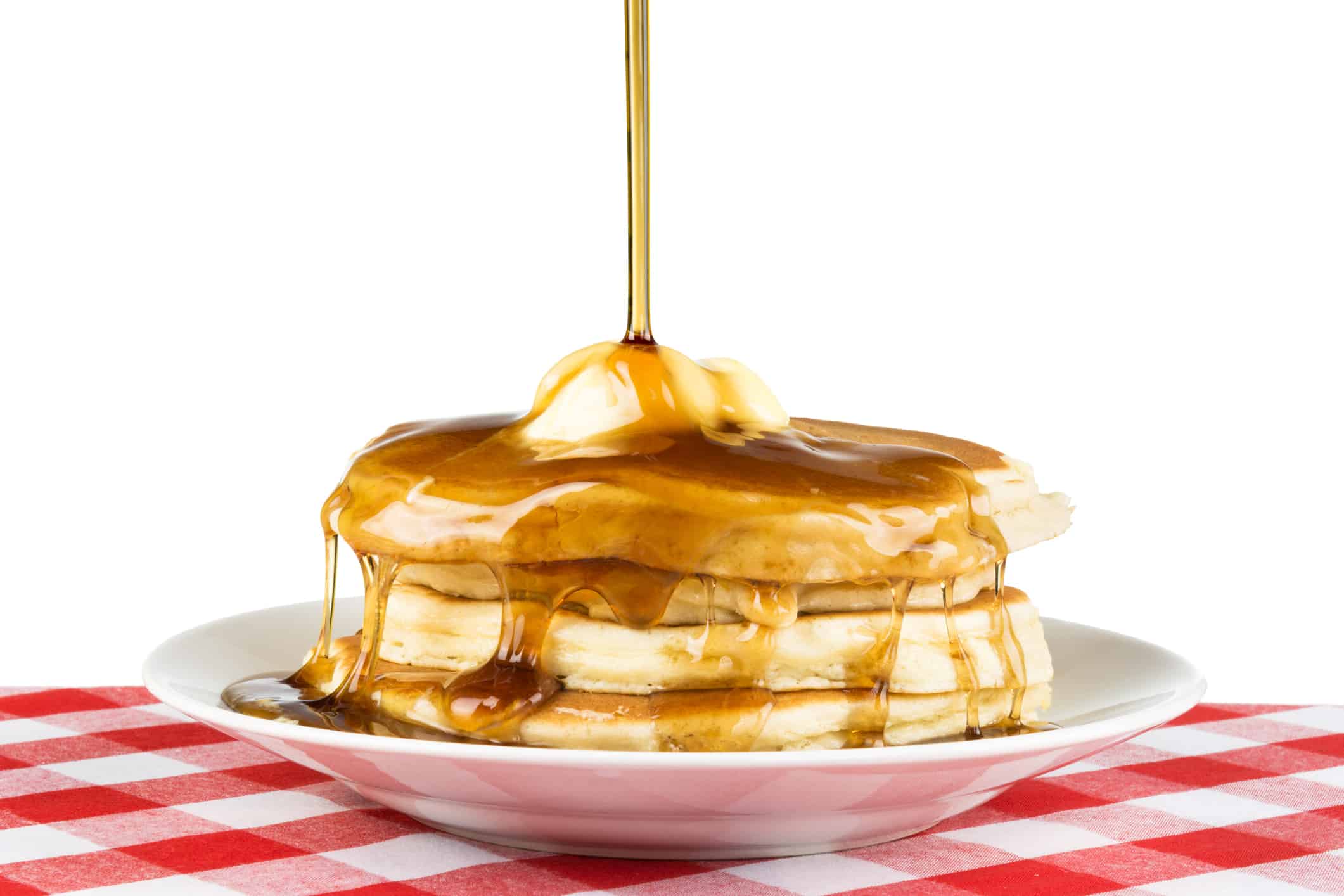 Sweet maple syrup being poured over a hot, freshly buttered stack of pancakes.
